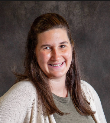 A woman wearing a white sweater and a green shirt is smiling for the camera.