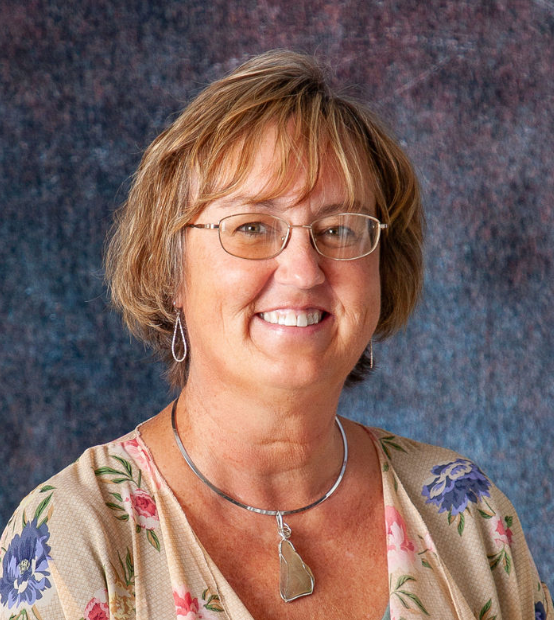 A woman wearing a black shirt and a necklace smiles for the camera