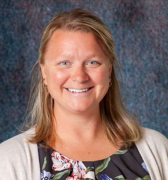 A woman wearing a blue shirt and a grey cardigan smiles for the camera