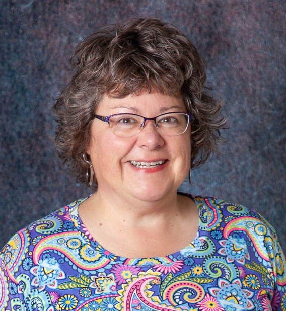 A woman wearing glasses and earrings is smiling for the camera