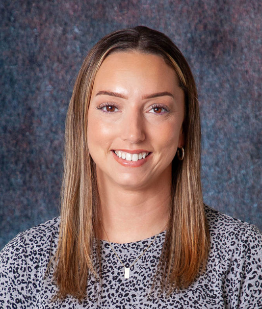 A woman with long hair and a necklace is smiling for the camera.