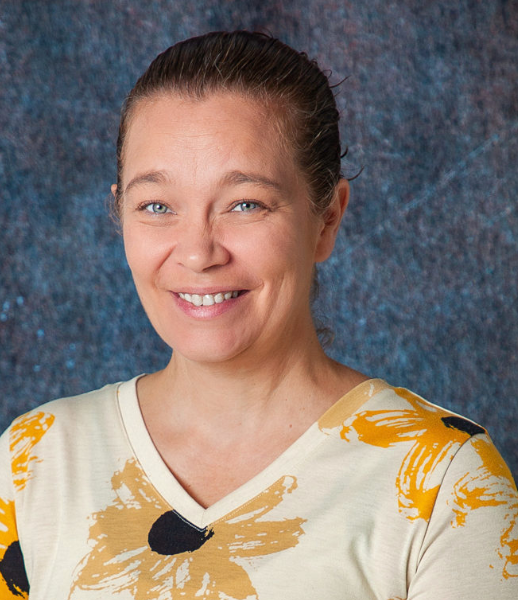 A woman wearing a floral shirt and a grey sweater smiles for the camera