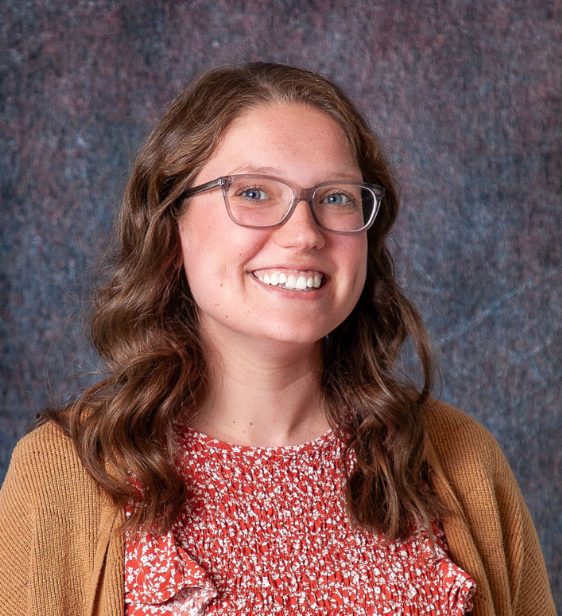 A woman wearing glasses and a purple sweater smiles for the camera