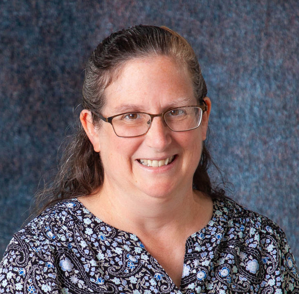 A woman wearing glasses and a purple sweater is smiling for the camera.