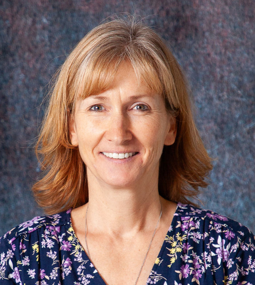 A woman with red hair is smiling and wearing a floral shirt