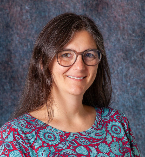 A woman wearing glasses and a white sweater smiles for the camera