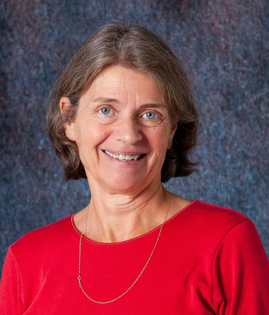 A woman wearing a blue shirt and a black vest smiles for the camera