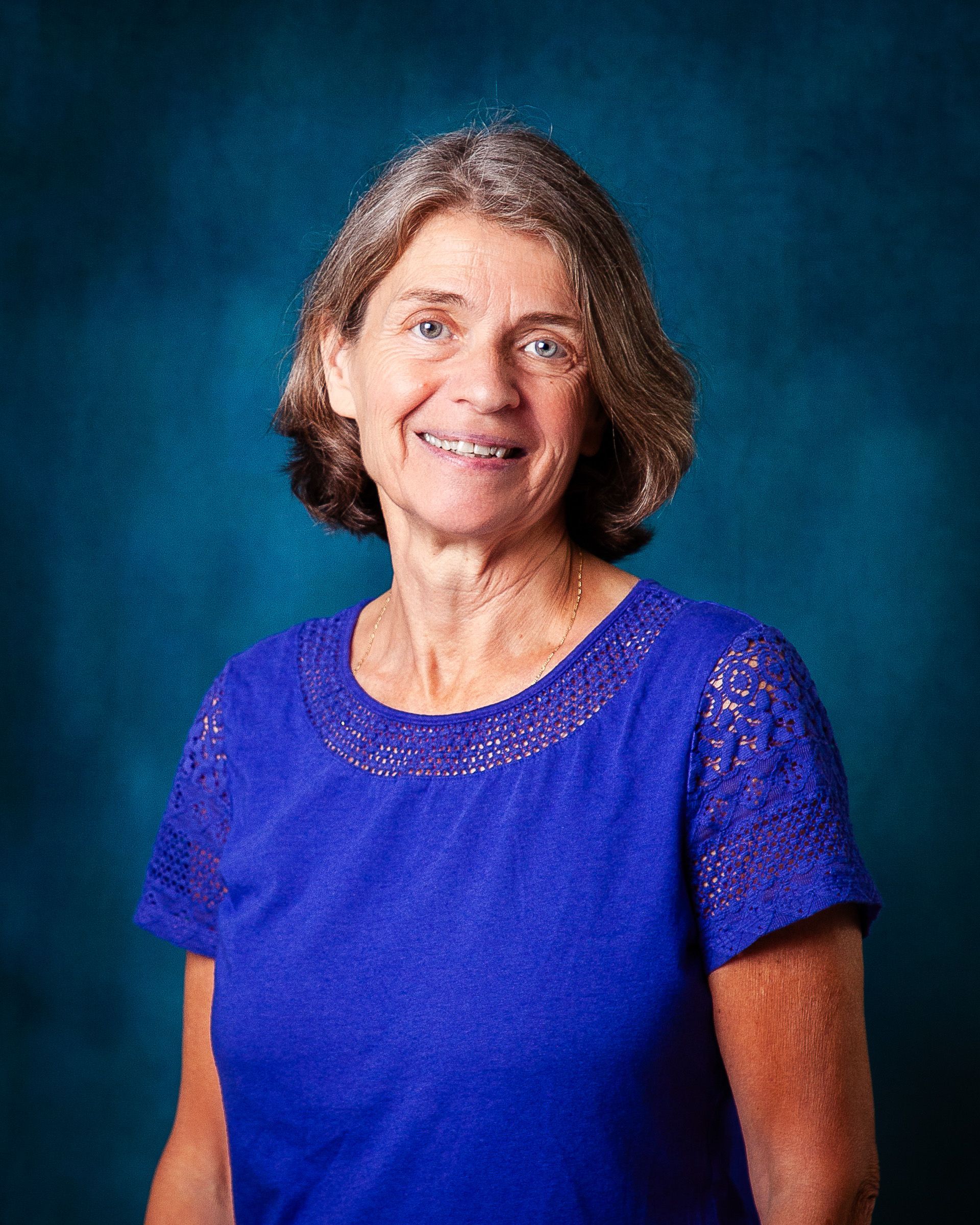 A woman wearing a blue shirt and a black vest smiles for the camera