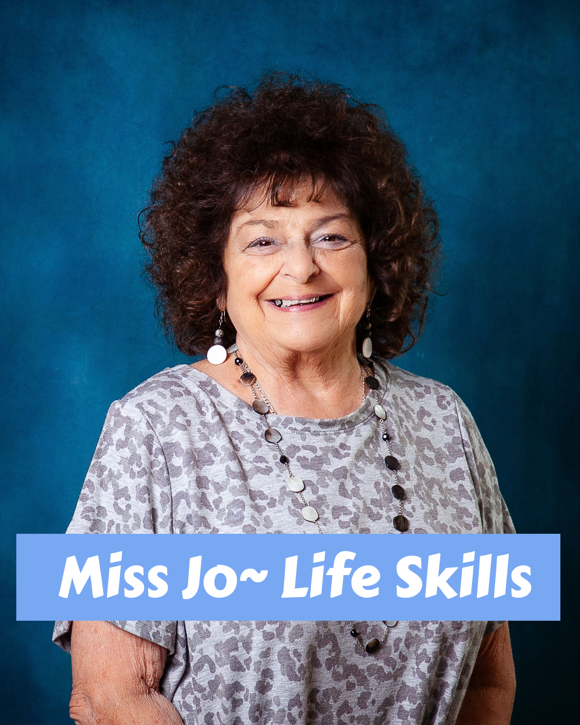 A woman with curly hair wearing a necklace and earrings smiles for the camera