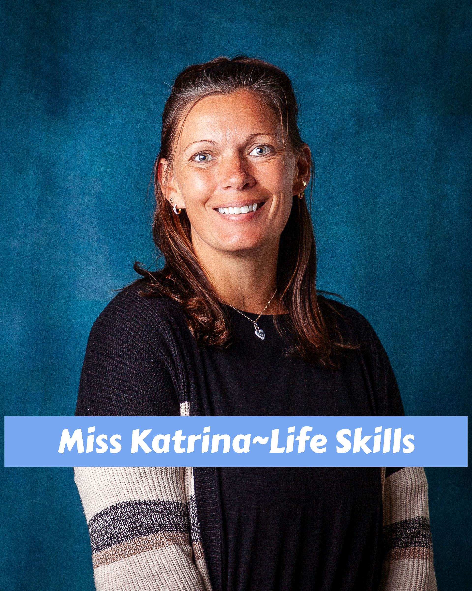 A woman wearing a pink sweater and a necklace is smiling for the camera.