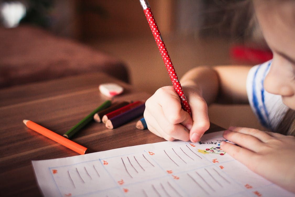 A child is writing on a piece of paper with a red pencil