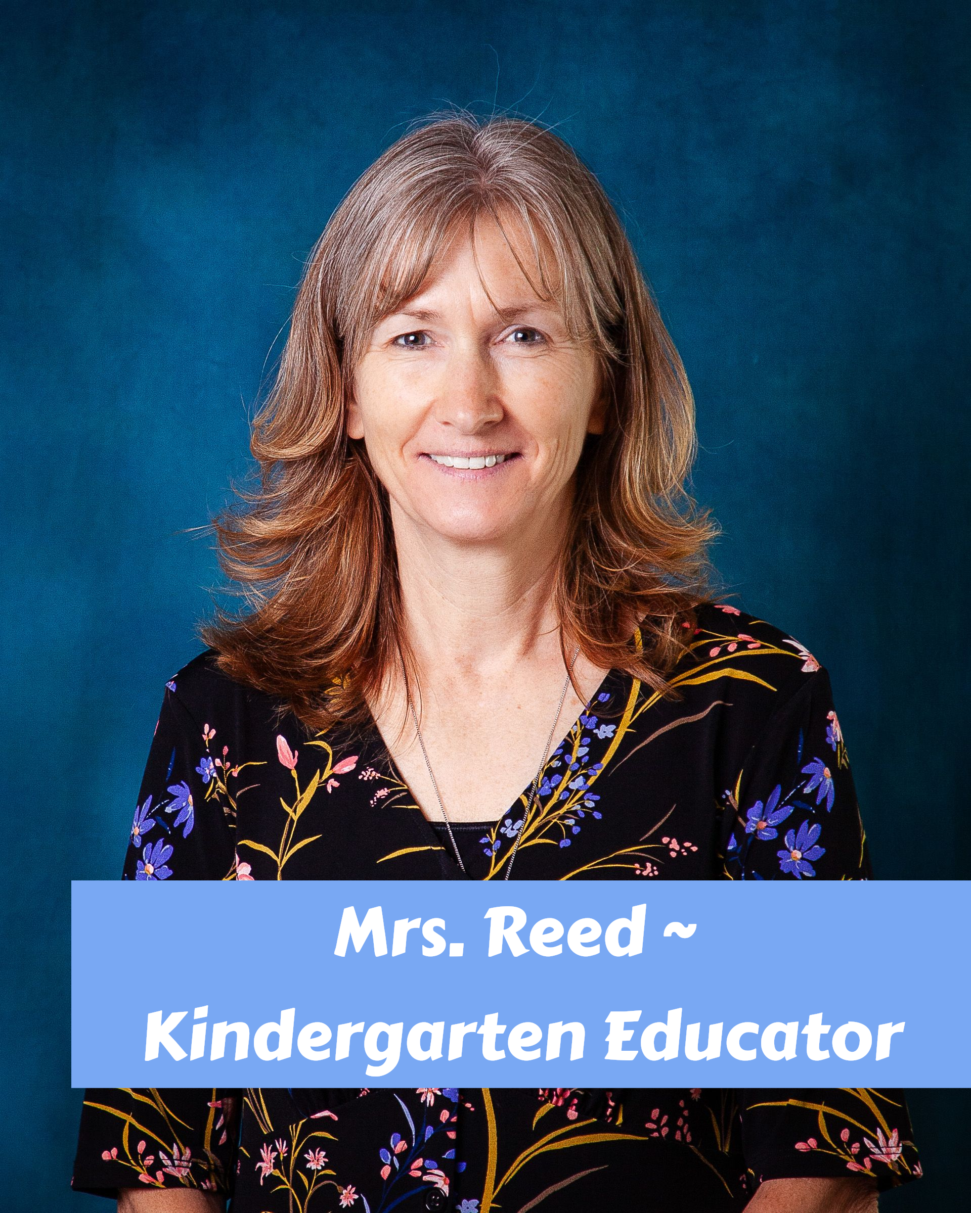 A woman with red hair is smiling and wearing a floral shirt