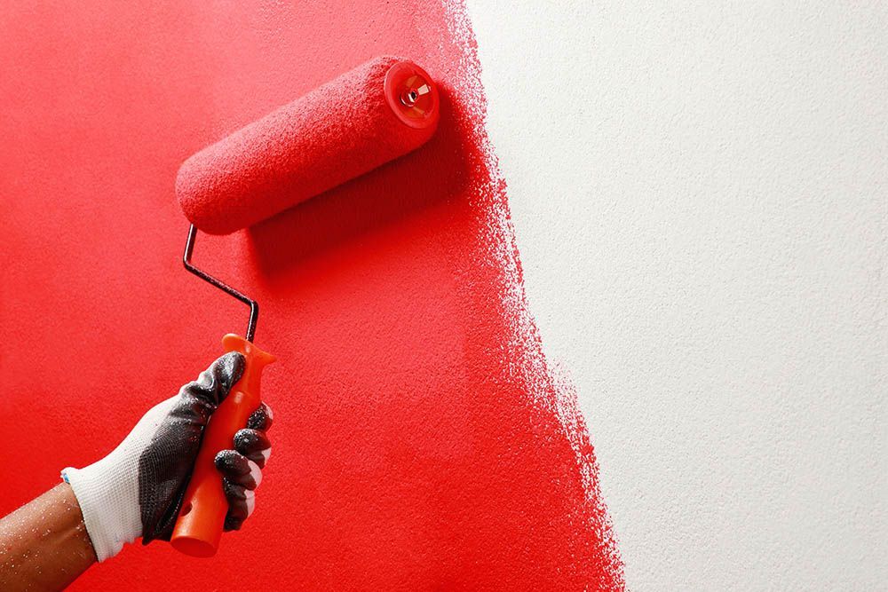 A person is painting a wall red and white with a paint roller.