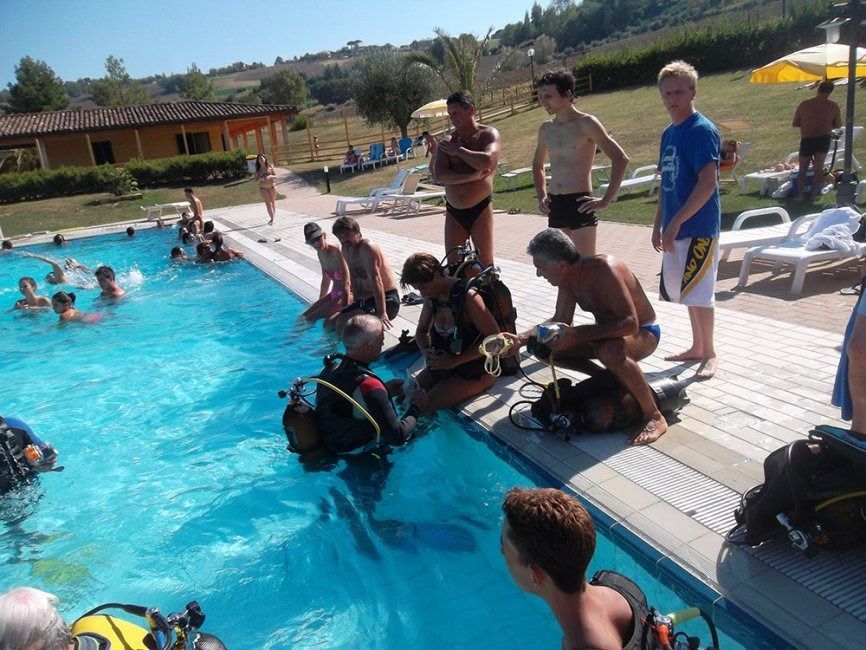 Lo chef in camice bianco e grembiule a righe sorride, seduto fuori.