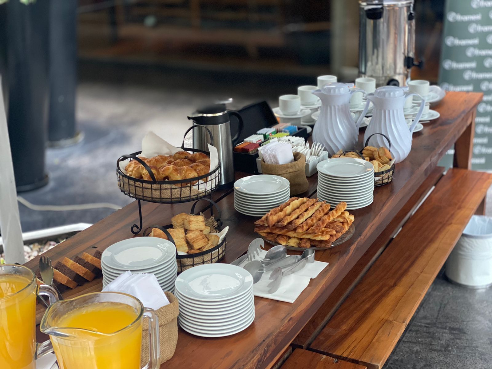 Una larga mesa de madera llena de platos y una jarra de jugo de naranja