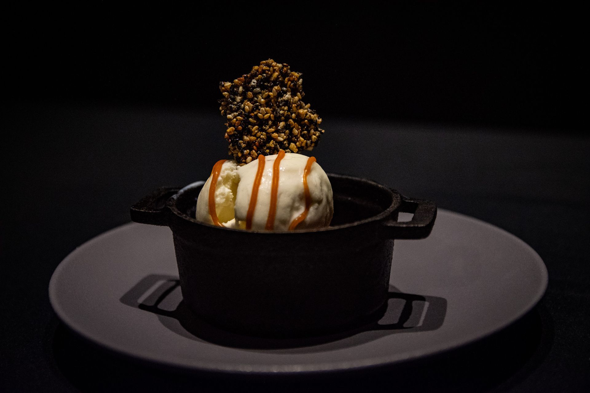 En un plato hay un cuenco de helado con salsa de caramelo encima.