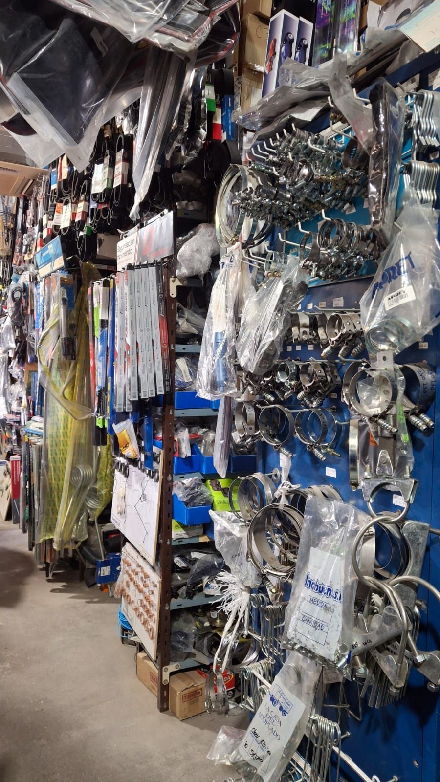 Una tienda de repuestos de autos desordenada, con artículos cromados y envueltos en plástico colgando de los estantes. 