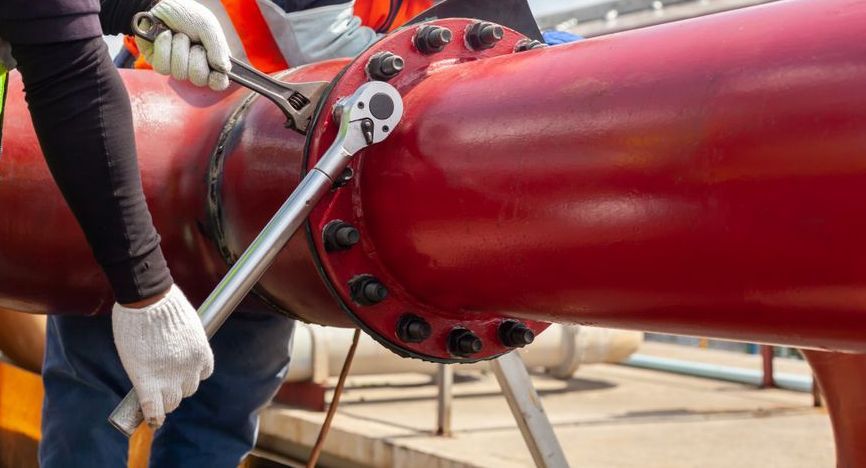 A Man is Working on a Red Pipe With a Wrench — J & N Plumbing Pty Ltd In Tamworth, NSW