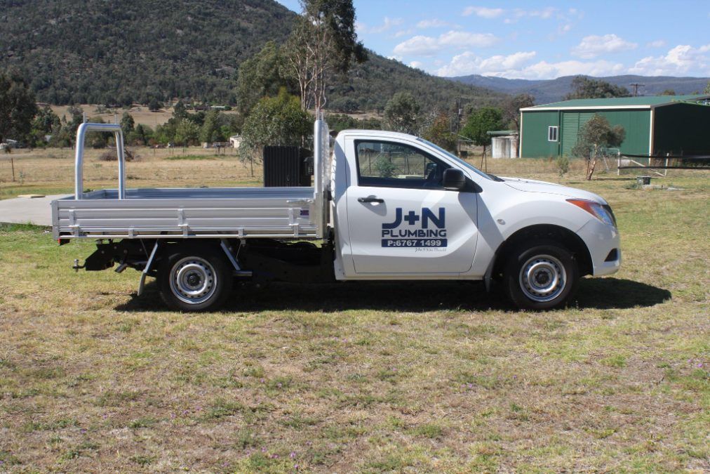 A White Truck With a Flat Bed is Parked in a Grassy Field — J & N Plumbing Pty Ltd In Tamworth, NSW