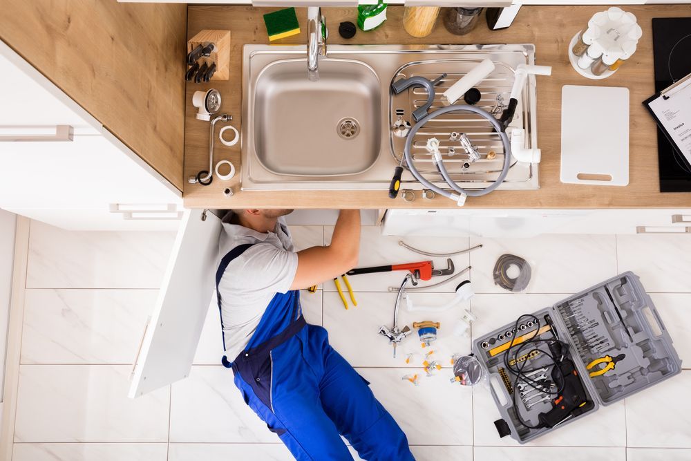 A Plumber is Fixing a Sink in a Kitchen — J & N Plumbing Pty Ltd In Armidale, NSW
