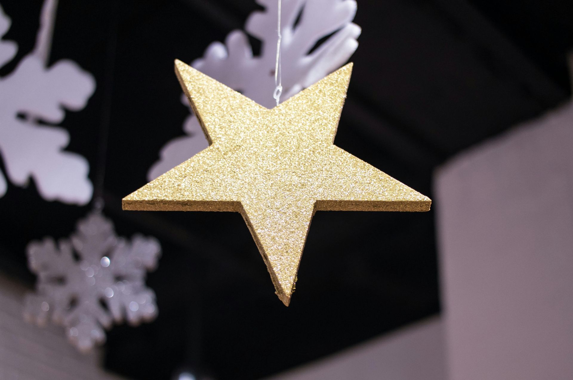 A gold star is hanging from the ceiling next to snowflakes.