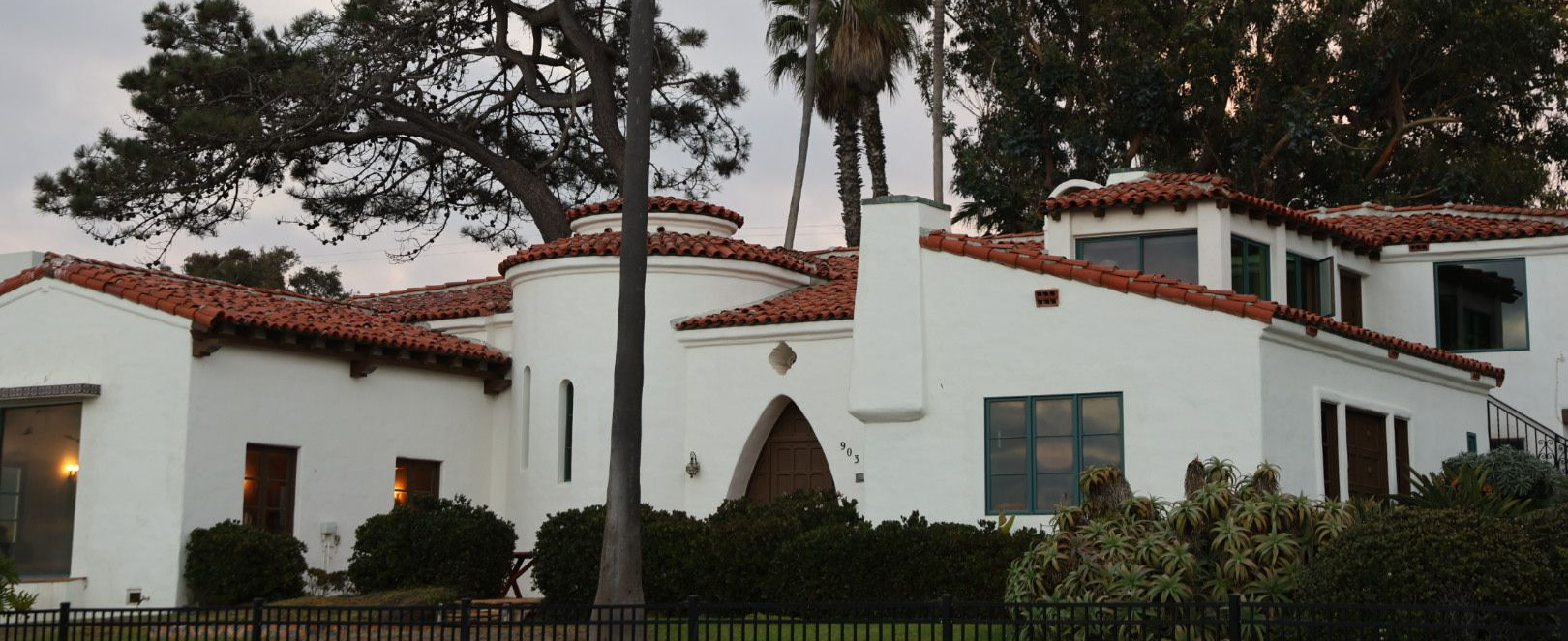 White stucco Spanish style house with red tile roof, surrounded by trees in Point Loma