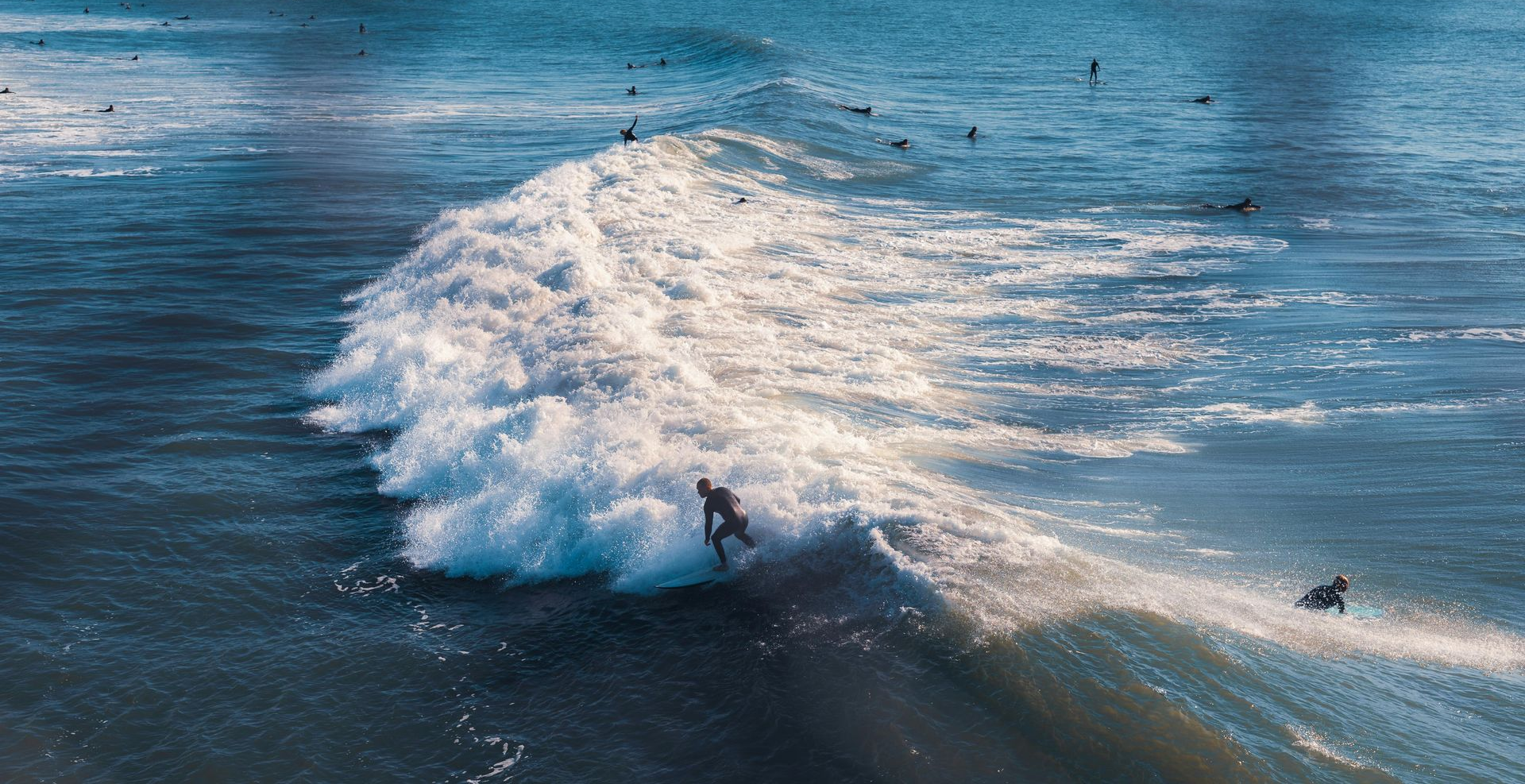 Aerial view of a surfer carving through a foamy wave on dark blue ocean water. Ocean Beach, San Diego 