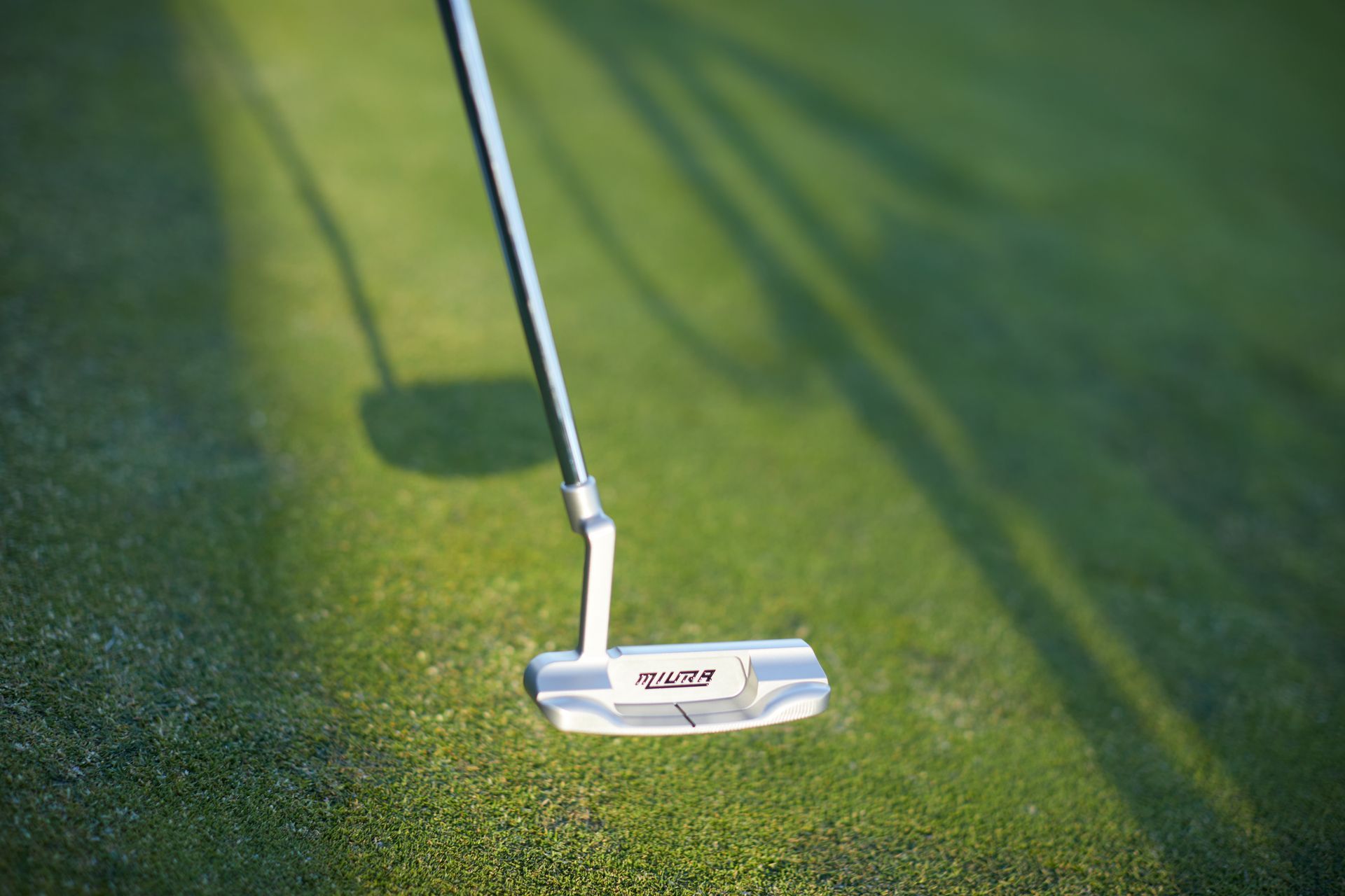 A golf ball is sitting on top of a golf course next to a golf club.