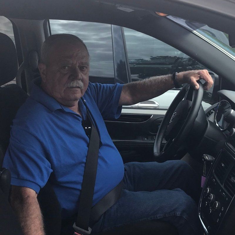 old man in blue t-shirt driving a car