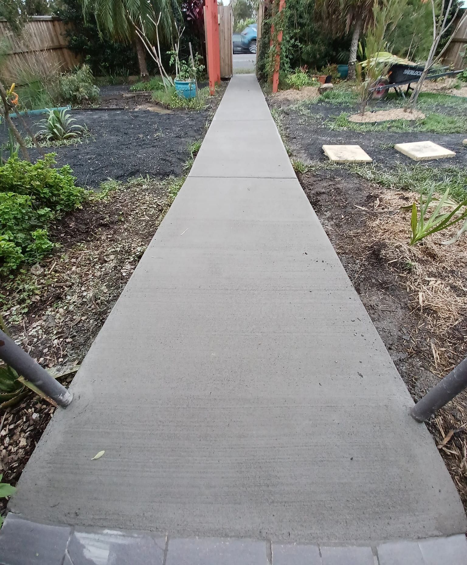 A Man is Working on a Concrete Driveway in Front of a House — Brocksolid Concrete in Pillar Valley, NSW