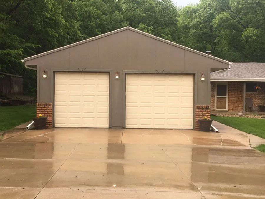 A garage with two white garage doors in front of a house.