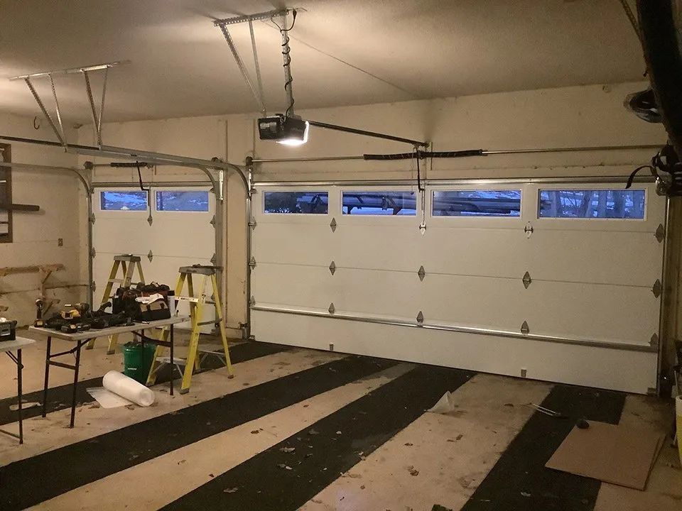 A garage with a garage door open and a table and ladder.