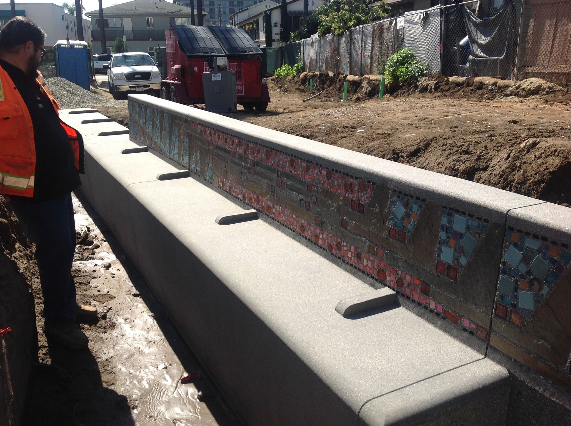 A man in an orange jacket is standing next to a concrete wall
