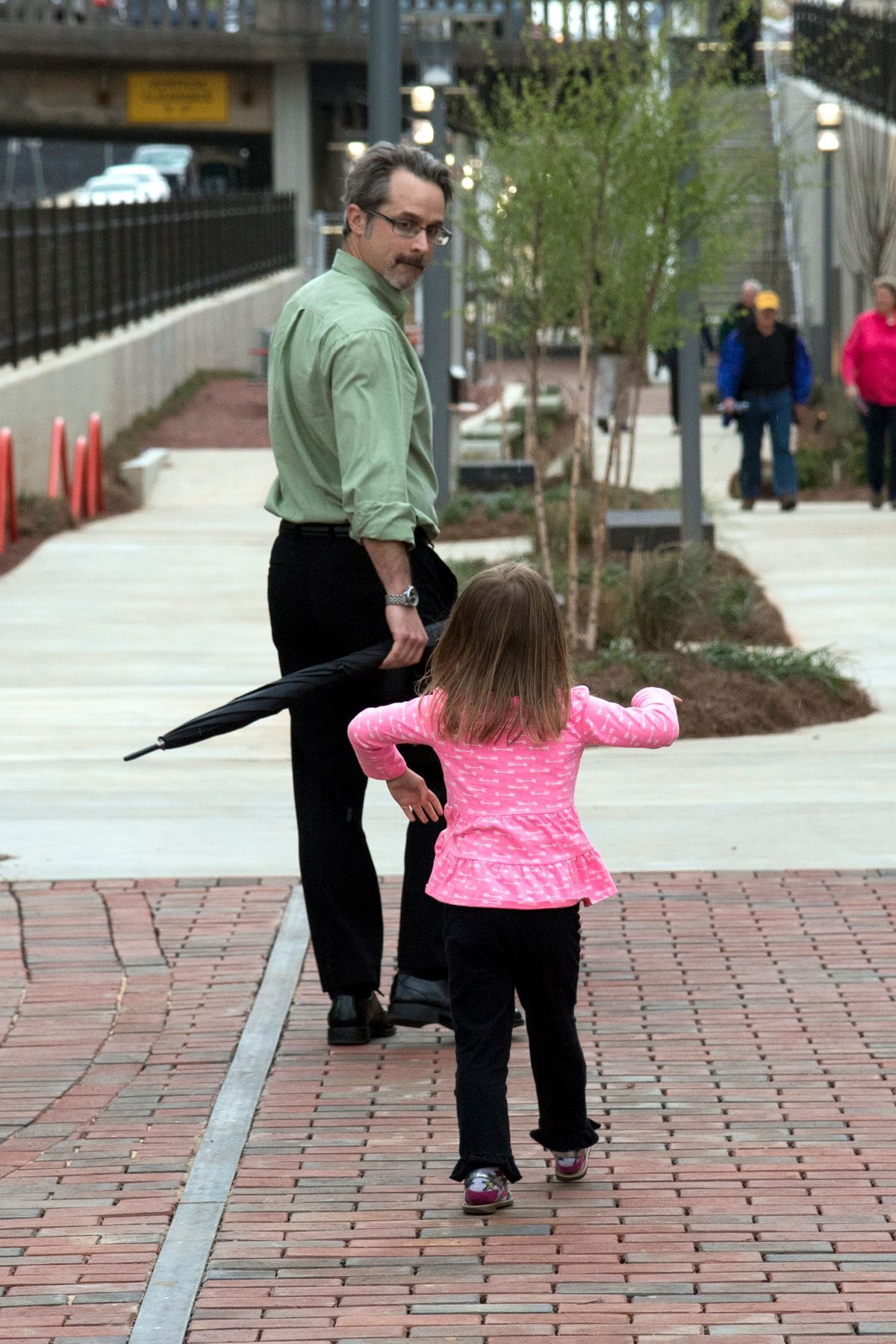 A little girl in a pink shirt is walking with a man holding an umbrella