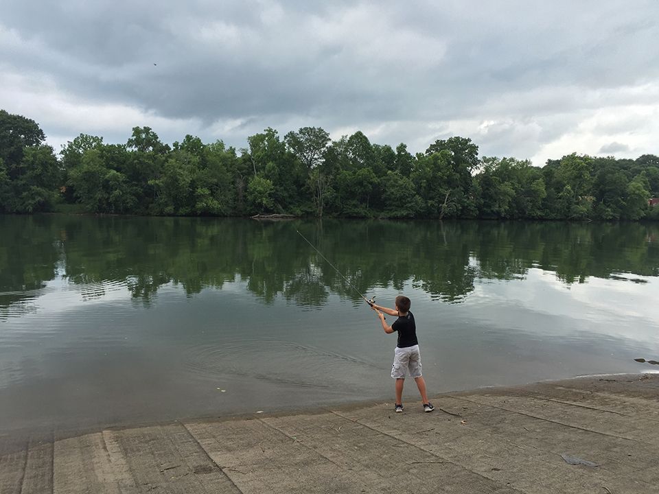 A young boy is fishing in a lake on a cloudy day.