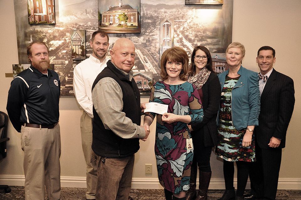 A group of people are standing around a woman holding a check.