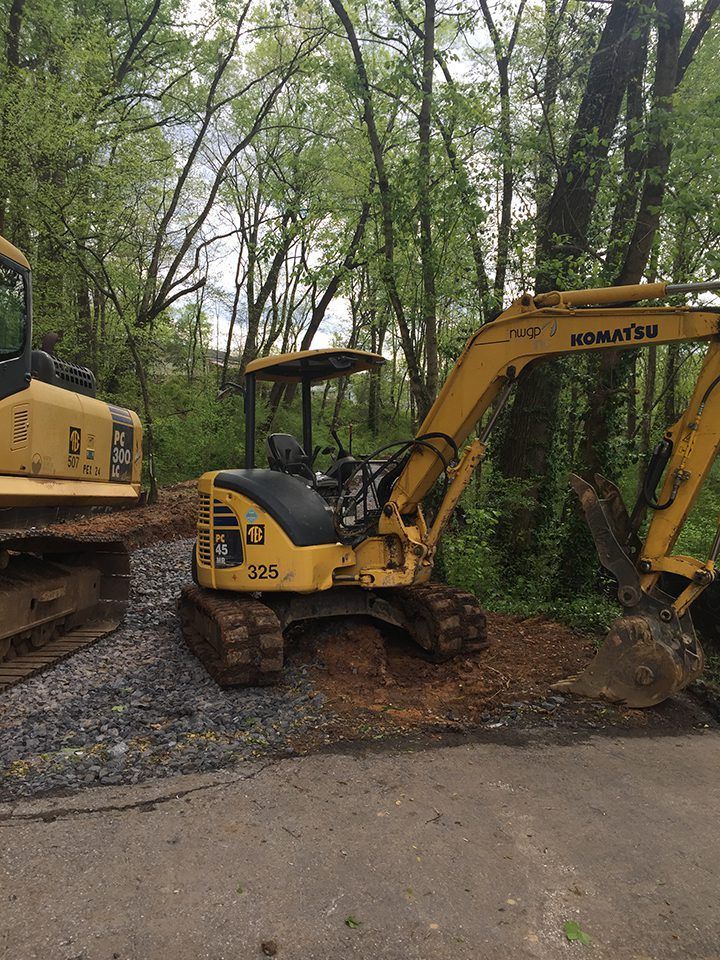 Two yellow excavators are parked on the side of a road in the woods.