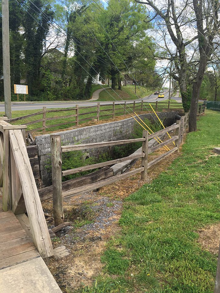 A wooden fence surrounds a small stream in a park.