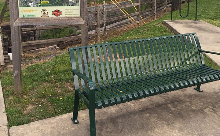 A green metal bench is sitting on a sidewalk next to a sign.