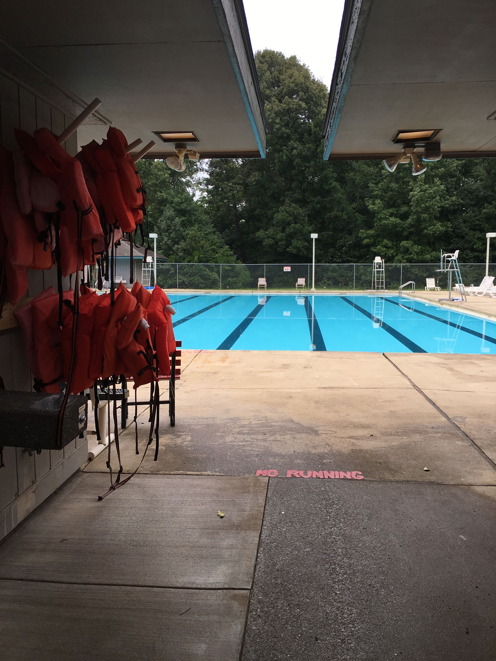 Life jackets are hanging on a rack in front of a swimming pool
