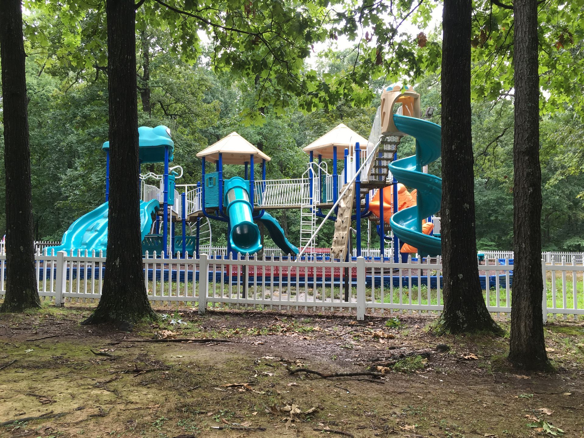 A playground is surrounded by trees and a white fence.