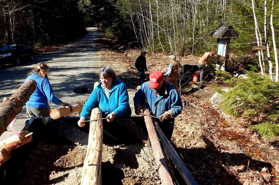 A group of people are working on a wooden structure in the woods.