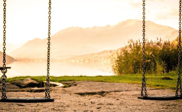 Two swings are sitting in the sand near a body of water.