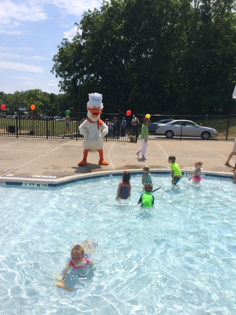 A group of children are swimming in a pool with a chef statue in the background
