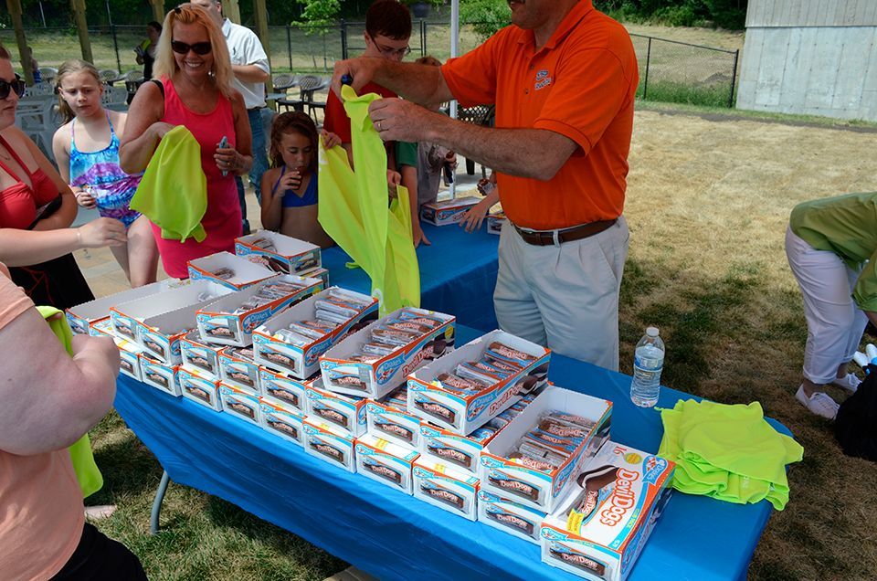 A man in an orange shirt is standing in front of a table full of yellow shirts