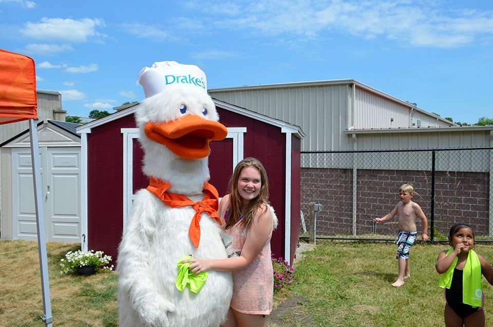 A woman is standing next to a duck mascot in front of a red shed.