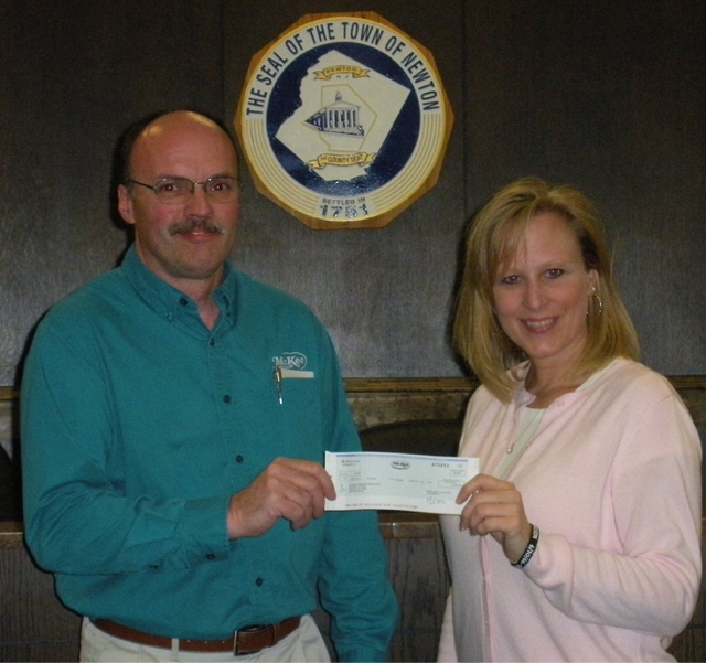 A man and woman holding a check in front of a seal that says the seal of the town of newton
