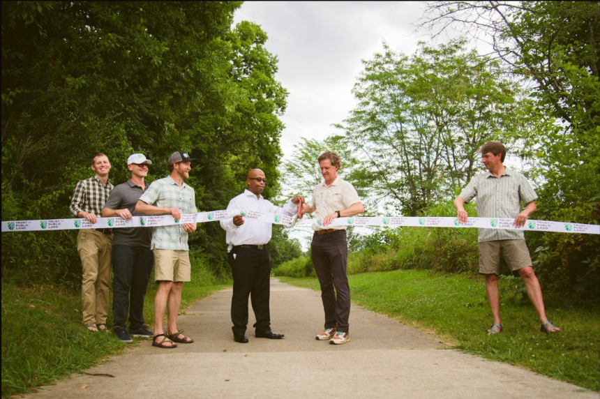 A group of men are cutting a ribbon on a path.