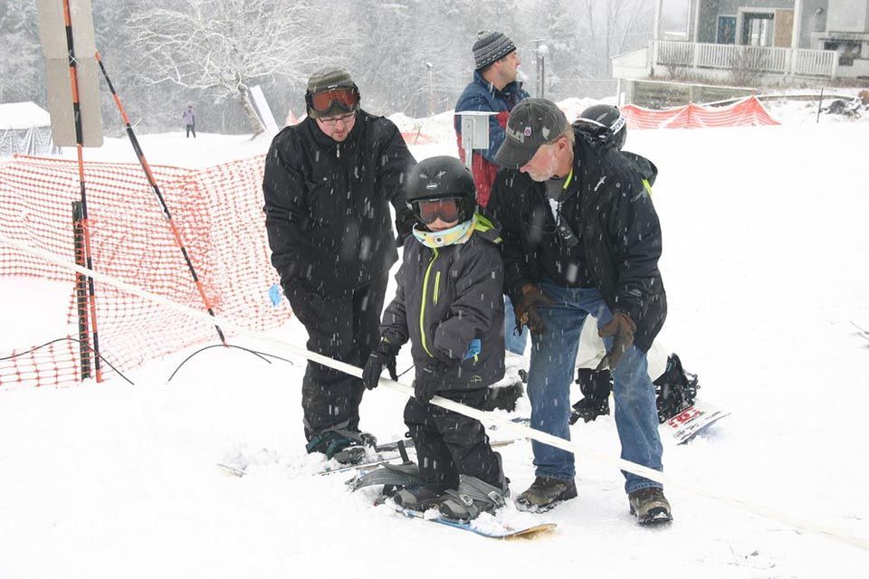 A group of people are standing in the snow with a child on a snowboard