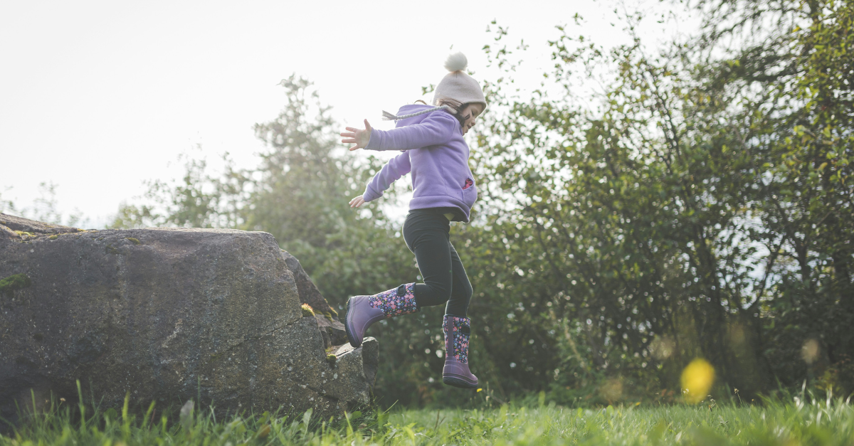 A little girl is jumping in the air in a field.